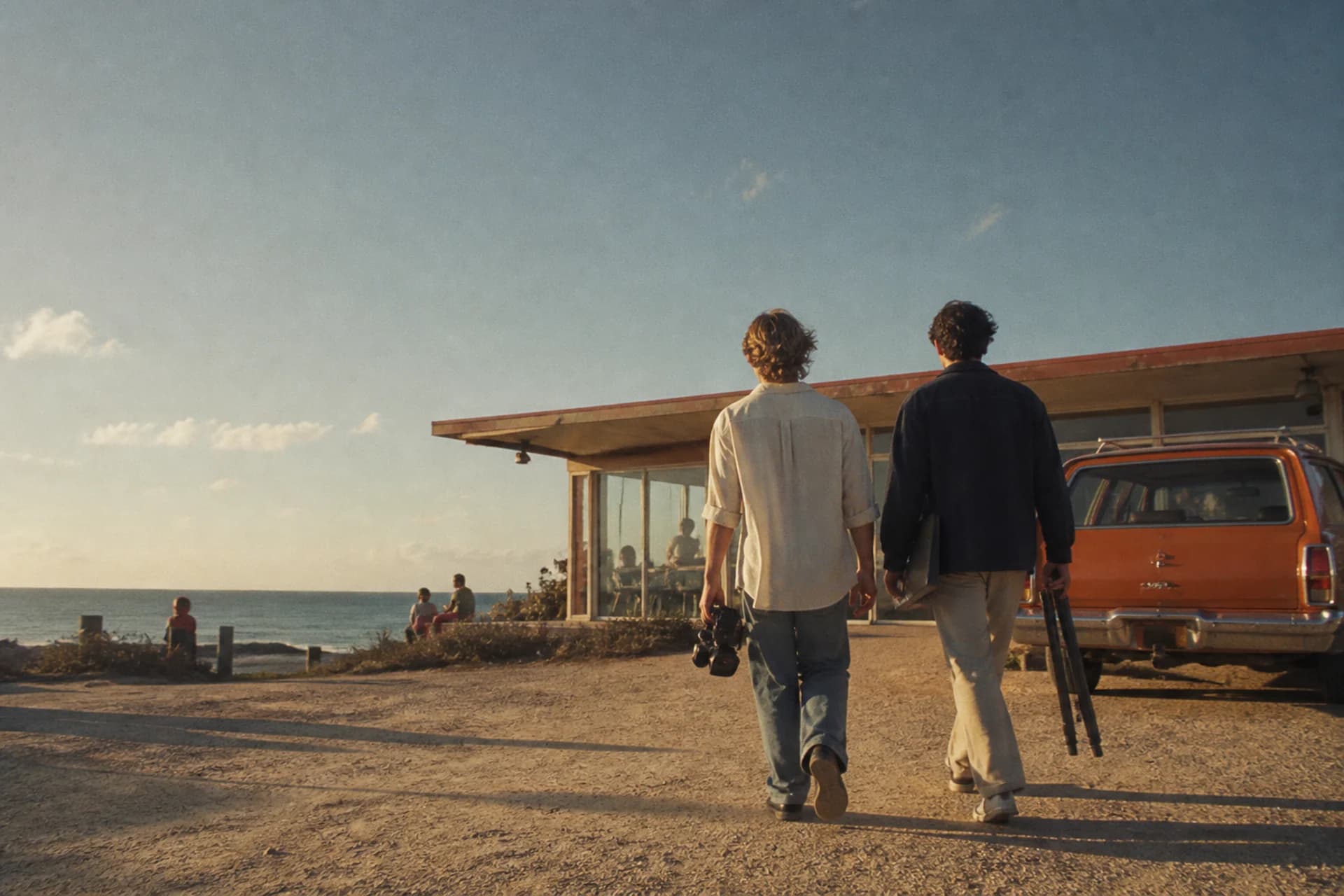 Grain-treated editorial image of two creatives walking toward a coastal location with camera equipment